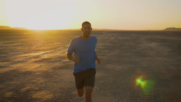 Athletic man working out with battle ropes on a dry lake at sunset