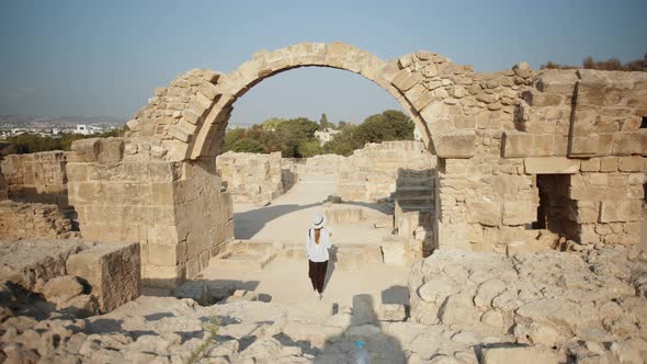 Woman in Summer Hat Walking Among Ruins of Ancient Buildings