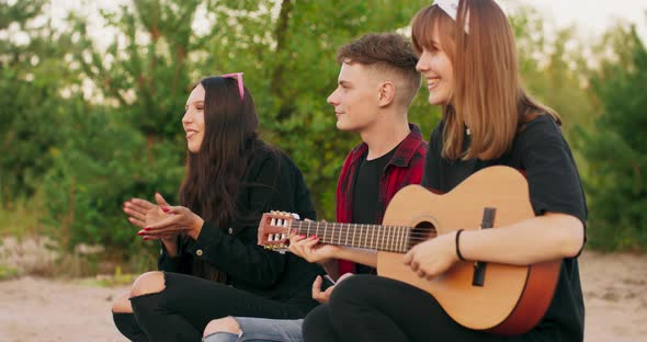 Young Men and Women are Singing Songs to the Guitar Resting Around Campfire and Enjoying Music and