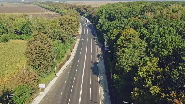 Cars move at highway road surrounded by green trees in a sunny day