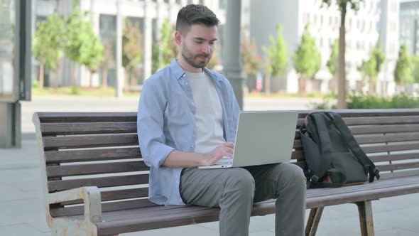 Young Man Pointing at the Camera While Sitting on Bench Outdoor