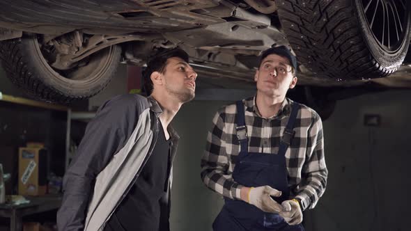 Handsome Auto Repair Technician Showing to His Maleclient the Main Problems with the Car