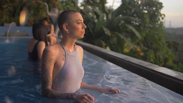 Gorgeous female tourist contemplatively poses in a tropical resort pool in summer