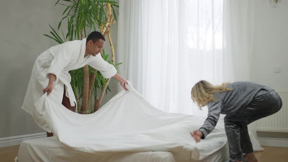 Wide Shot of Happy Smiling Couple Making Bed and Lying Down Talking