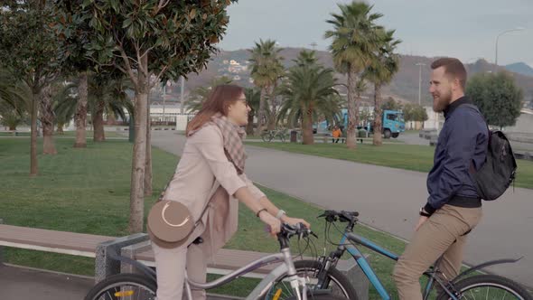 Male and Female Friends Are Meeting During Bicycle Walking in Park Chatting