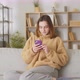 Attractive Teenage Girl Sitting on the Sofa at Home Using Phone and Smiling - VideoHive Item for Sale
