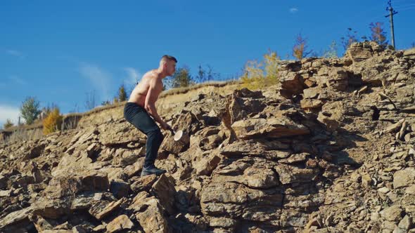 Side view of a strong man breaking stones with a hammer. Shirtless athletic man exercising with a sl