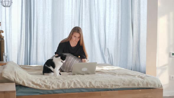 Girl Is Working on a Grey Laptop on Bed with Big Cat
