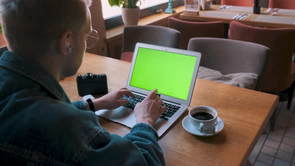 Rear View of a Young Male Freelancer Sitting at the Table in a Cafe and Working