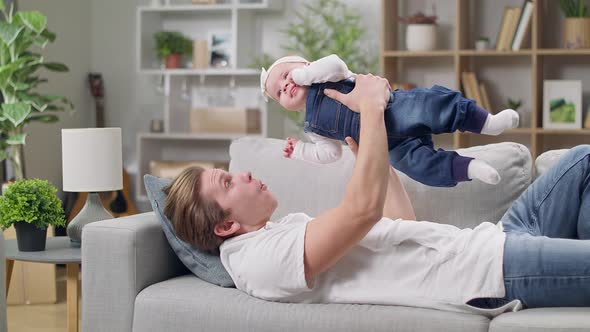 Dad Raises His Little Daughter Lying on the Couch Not