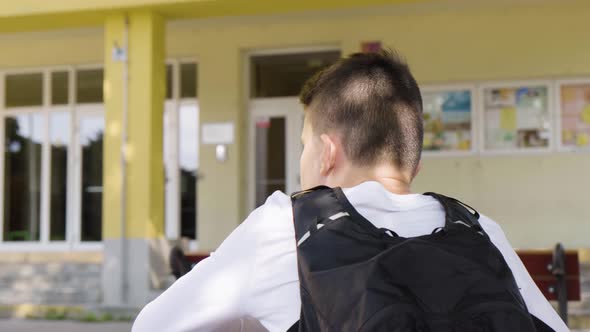 A Caucasian Teenage Boy Looks Around As He Sits in Front of School  Rear Closeup