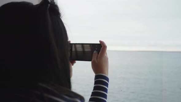 Back view of Asian woman taking a picture through the window on boat