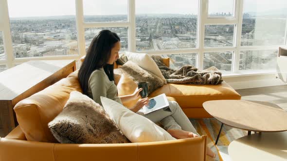 Woman using digital tablet while having coffee in living room