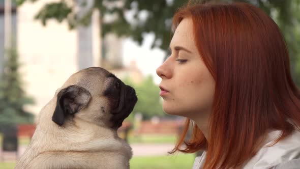 Girl Trying To Kiss Her Pug and Looking at Camera