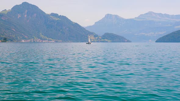 Sailing boat on Lake Lucerne in the background of forested mountains on a sunny day.