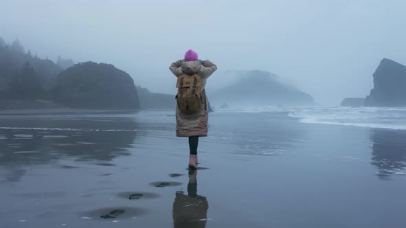 Aerial Tourist with Backpack Walking By Wet Surface of Ocean Beach on Cloudy Day