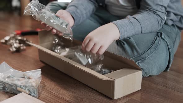 Hands of Boy Take Out Fittings for Furniture Assembly From Box Closeup