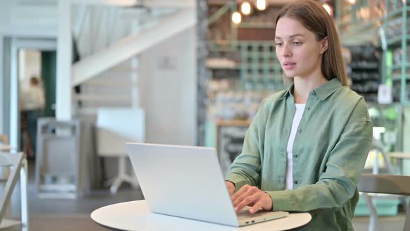 Focused Young Woman Working on Laptop in Cafe