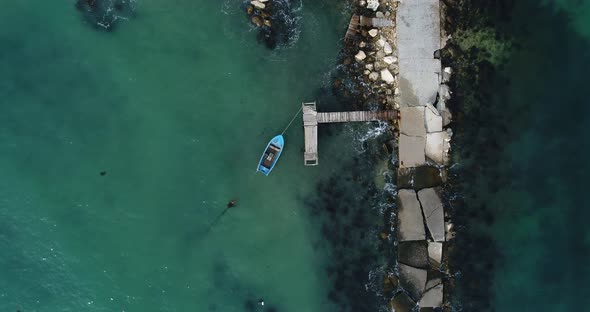Aerial video of lonely fishing boat and wooden pier in turquoise ocean, sea. Top down view