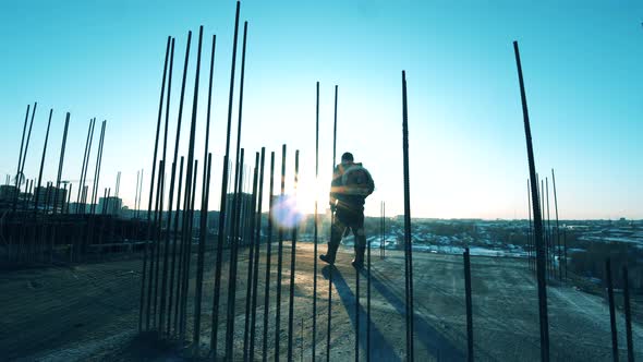 Worker Is Walking Along the Open Construction Site with a Hammer. Construction Worker at a