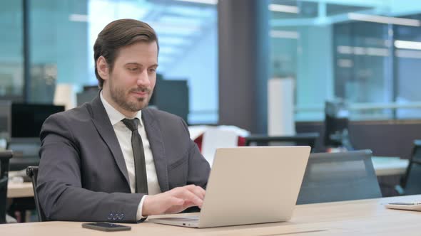 Businessman Showing Thumbs Down Sign While Using Laptop in Office