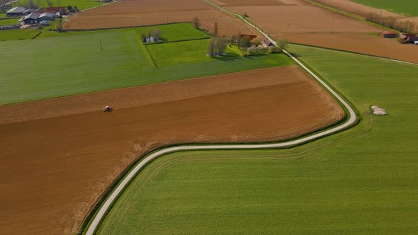 Aerial view of the countryside. A tractor plows the field next to the road. The village and the chur