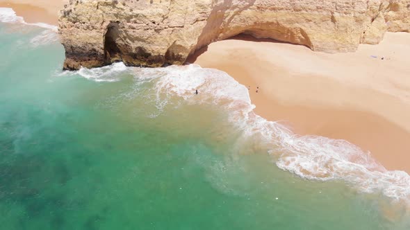 Aerial flying backwards over clear turquoise beach with rock formation, Algarve