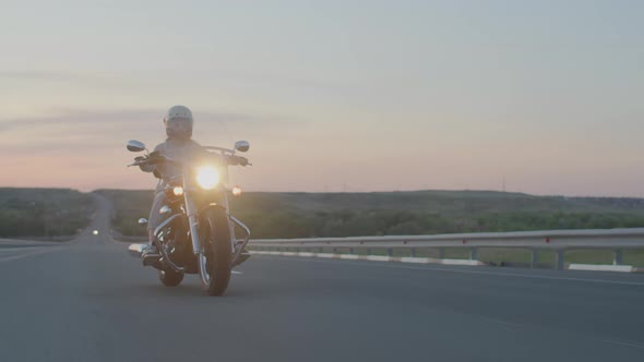 Confident Woman Rides Motorcycle Highway in Helmet with Headlight on Against Sunset