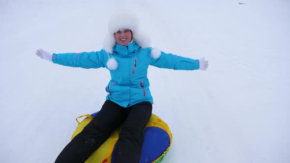 Beautiful Young Woman Slides Slide in Snow on an Inflatable Snow Tube and Waves Hand. Happy Girl