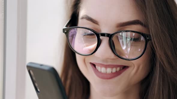 Beautiful Woman in Glasses Is Near the Window Smiling