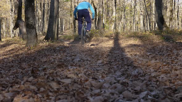 Slow-motion of a man on a mountain bike racing through the leaves in the forest