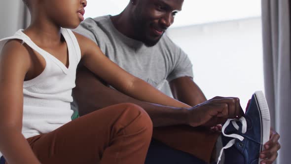 African american father helping his son with getting dressed in bedroom