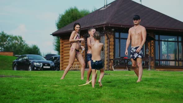 Family in the Backyard of a Country House in the Summer Relax Playing with Water and Hosing