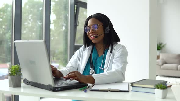 Professional African American Female Doctor in White Medical Coat and Headset Making Conference Call