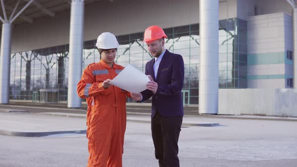 Young Architect in a Black Suit Examining the Building Object with Construction Worker in Orange