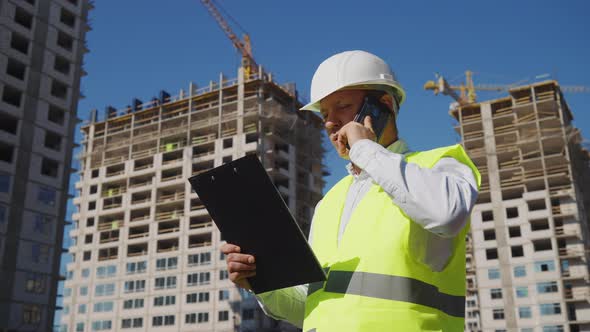 Foreman Checking Plans and Talking on Phone on Construction Site