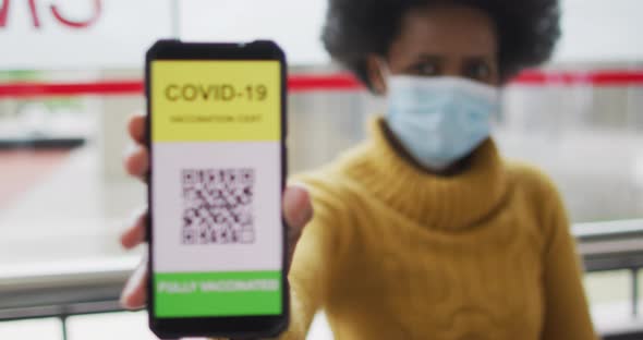 African american businesswoman with face mask preparing covid 19 certification on smartphone