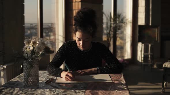 Young Sophisticated Female Artist Drawing with a Pen Siting By the Table in Art Studio with Wide