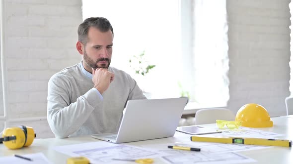 Pensive Young Architect Using Laptop in Office