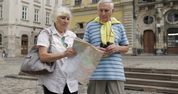 Senior Male and Female Tourists Walking with a Map in Hands Looking for Route