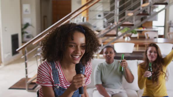 Diverse group of female friends having fun singing karaoke and drinking beer at home