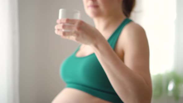 Pregnant Woman Holds a Glass of Water in Her Hand
