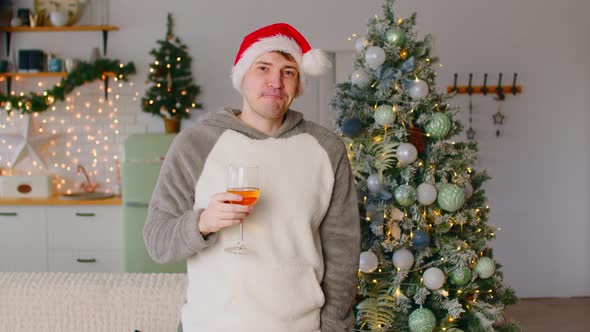 Man in Santa Hat Drinking Wine Near Christmas Tree in Living Room