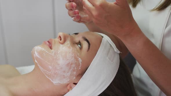 Caucasian woman lying back while beautician gives her a facial