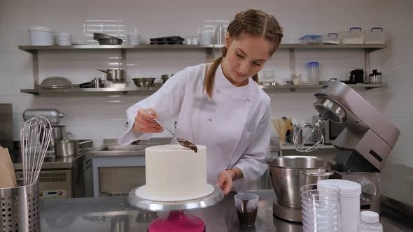 A Pastry Chef Pouring Liquid Chocolate From a Spoon on a White Cream Sponge Cake