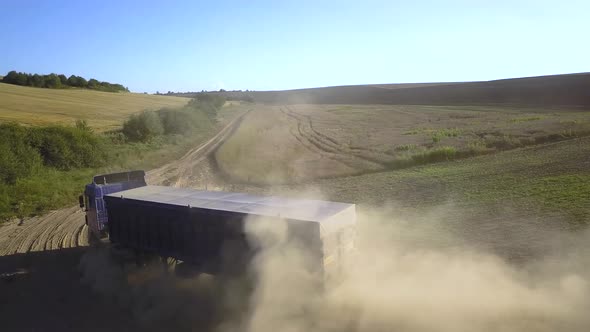 Aerial view of a truck driving on dirt road between plowed fields making lot of dust.