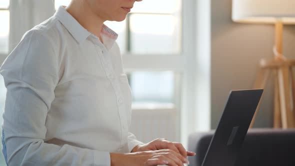 Woman with Glasses Is Sitting on the Couch in a Cozy Room and Working on a Laptop. Concept of Remote