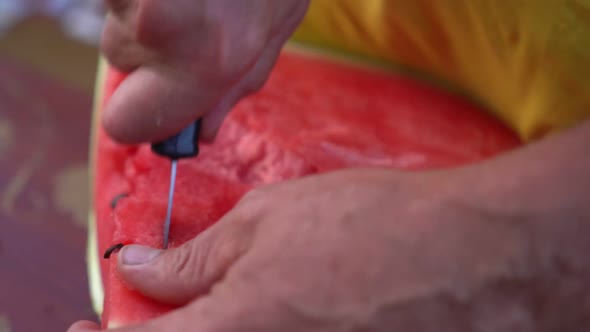 Country man in yellow t-shirt cuts red watermelon with knife