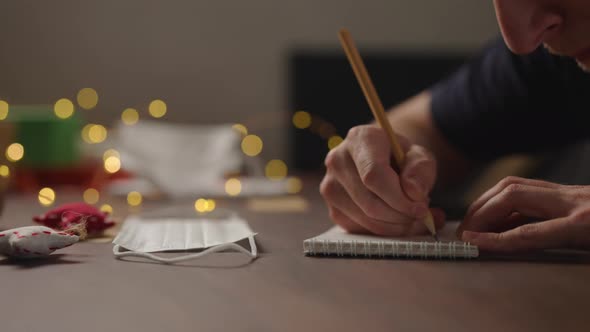 Slow Motion Orbit Shot Closeup Man Writes Shopping List Notepad Pencil Under Warm Light Evening