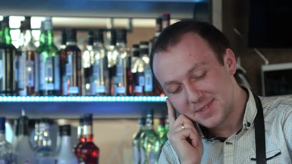 Happy Barman in Apron Calling on Smartphone at Bar